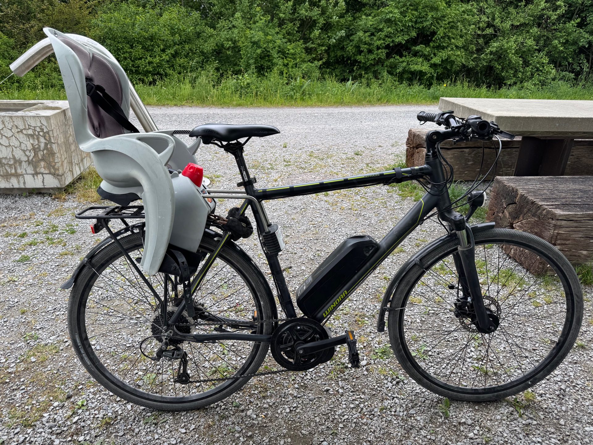 The converted bike parked on gravel at a picnic spot with a child seat mounted on the rear rack