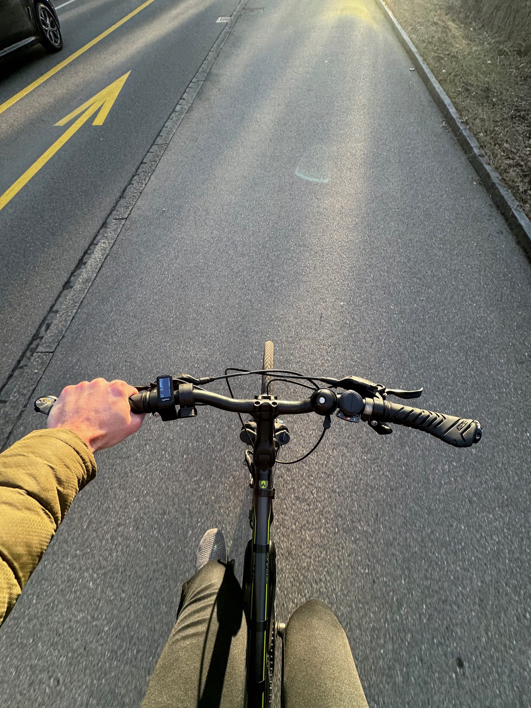 A first-person view over the handlebars riding along a road bike lane in low winter sun, the EggRider display by the left grip