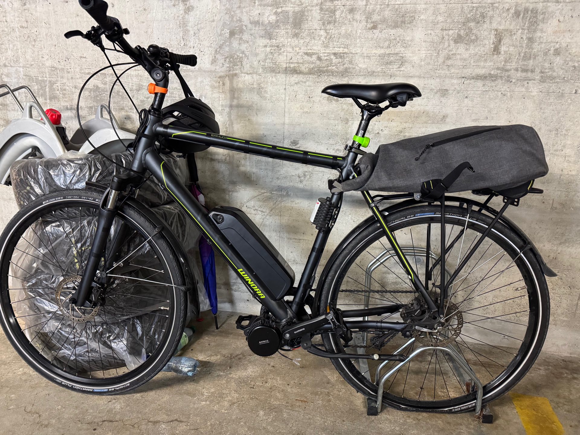 The bike parked in a garage with mudguards, a rear pannier rack and a grey pannier bag fitted