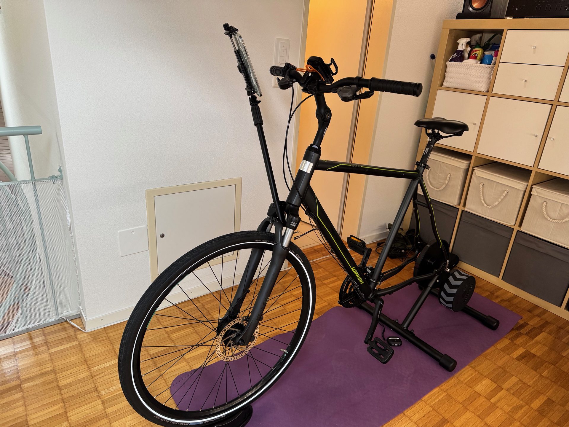The bike set up on an indoor turbo trainer on a yoga mat in a living room, with a phone mounted on the handlebars